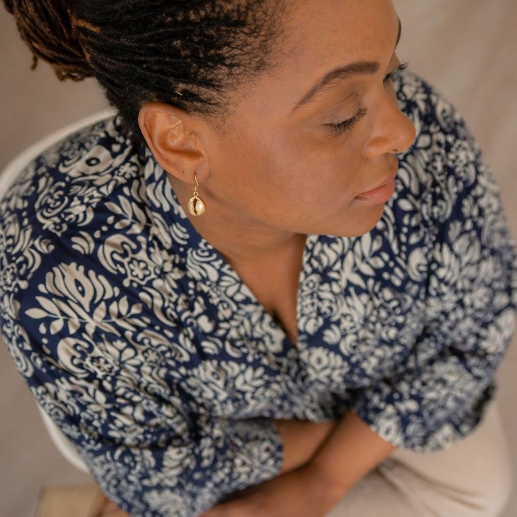 femme en chemisier blouse bleu et pantalon beige portant des boucles d'oreilles pendantes cauris